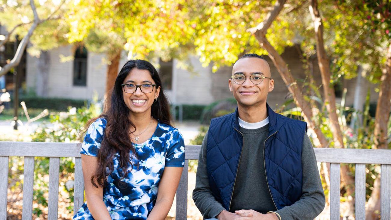 Two students sit on bench smiling